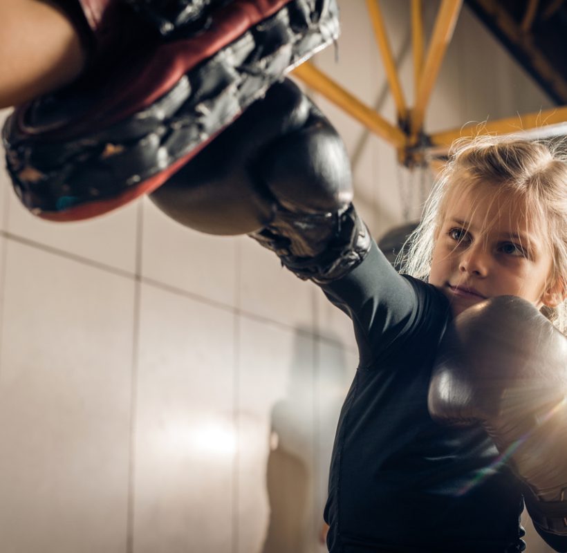 Small girl exercising boxing with unrecognizable coach in a health club.